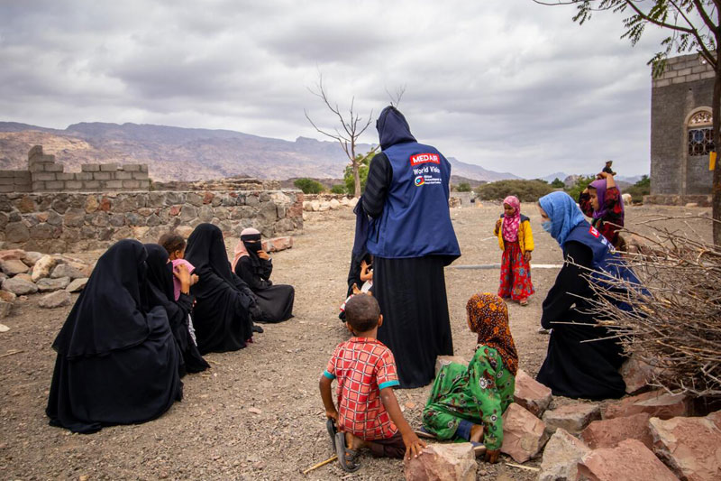 Yemeni women and children sitting on the ground outdoors.