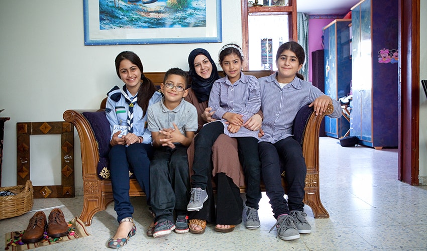 Woman in headscarf sits on couch surrounded by four children.