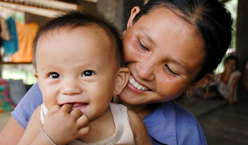 In Laos, a mom holds her baby close to her and beams with joy while looking at him.