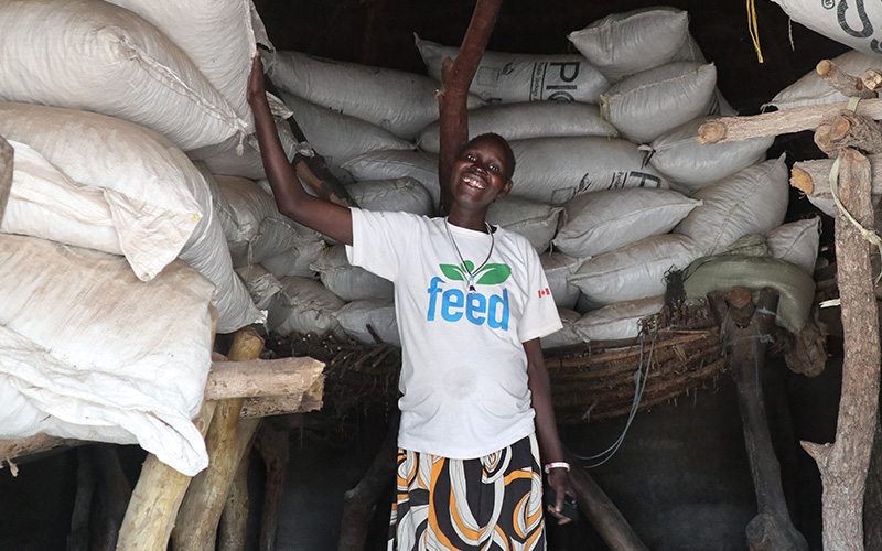 A woman stands proudly in a barn filled with big bags of groundnuts.