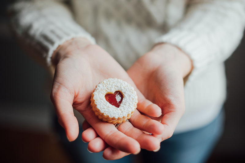 An image of hands holding a heart shaped cookie delicately.