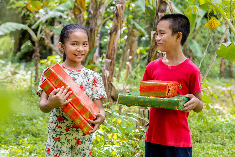Two children posing happily outside, while holding wrapped Christmas gifts.