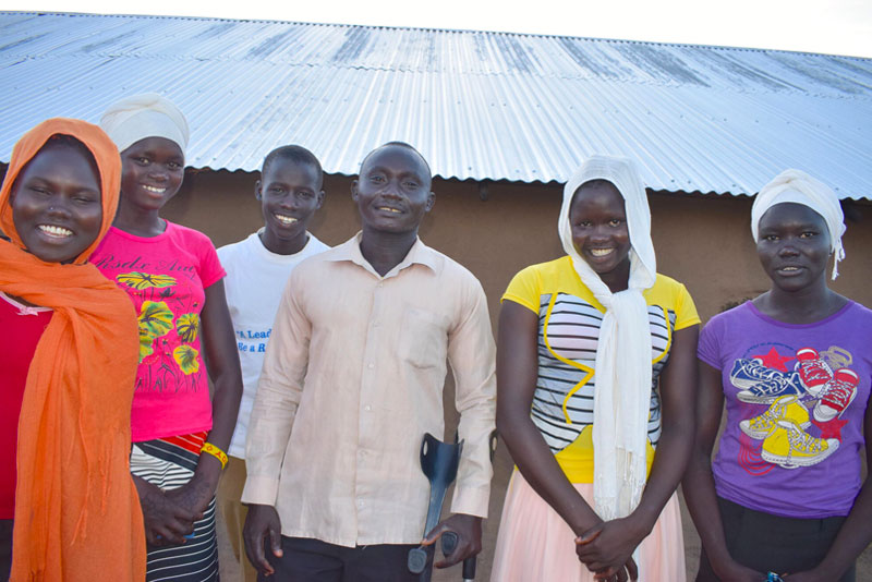 A group of World Vision community club members stand together and smile joyfully.