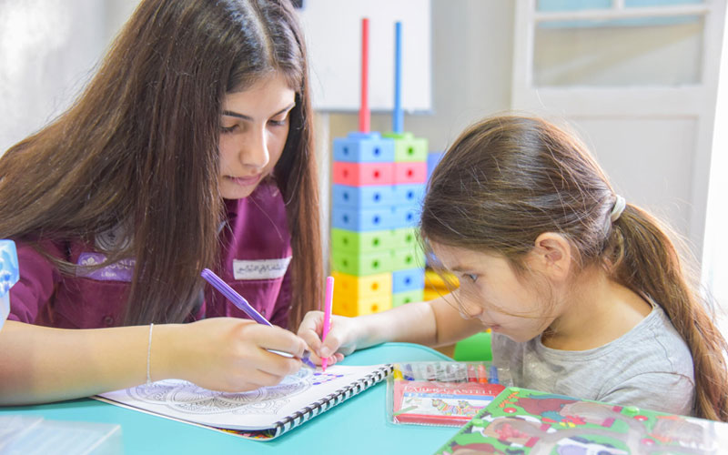 A woman and young girl are seated in a children’s space, coloring in a book together.