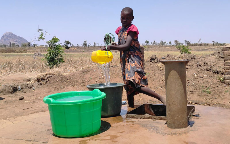 A young girl in a rural area fills two large buckets with water from a well.