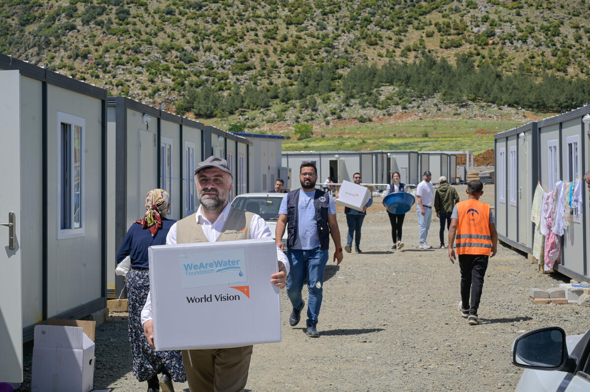 World Vision staff walk around an outdoor crisis relief center distributing emergency supplies to those in need.