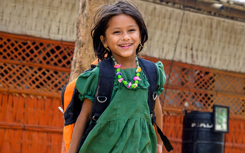 A little girl in a green dress smiles for the camera.