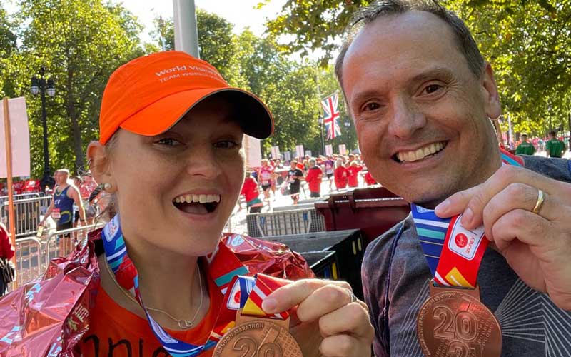 Both smiling, a young woman and a man hold up gold medals printed with London Marathon 2021.