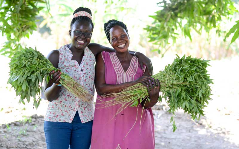 Two women smiling while holding vegetables.