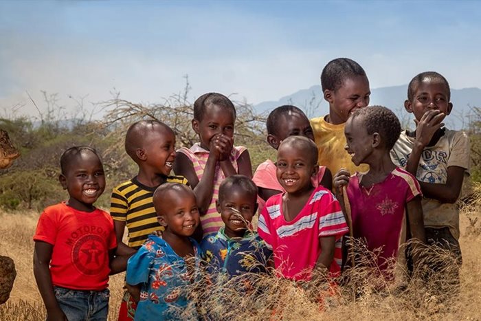In Soin, Kenya, 10 children in colourful t-shirts stand in a field, smiling at the camera.