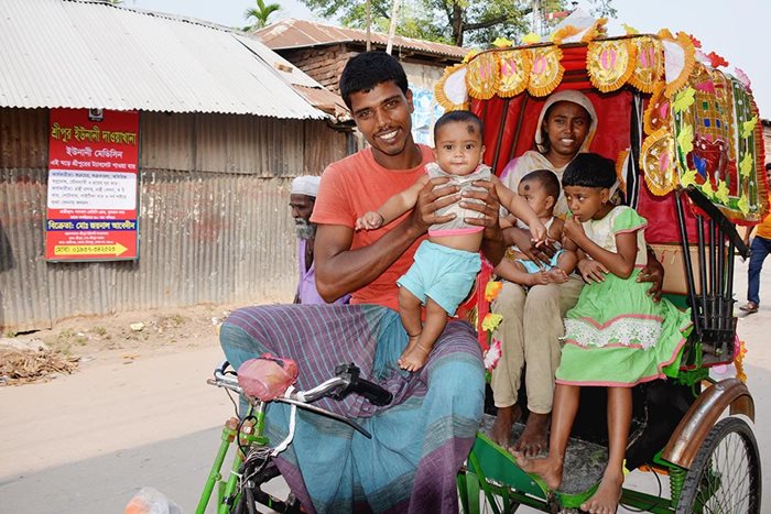 A man, woman and three children ride in a colurful rickshaw along a road in Bhandaria, Bangladesh. 