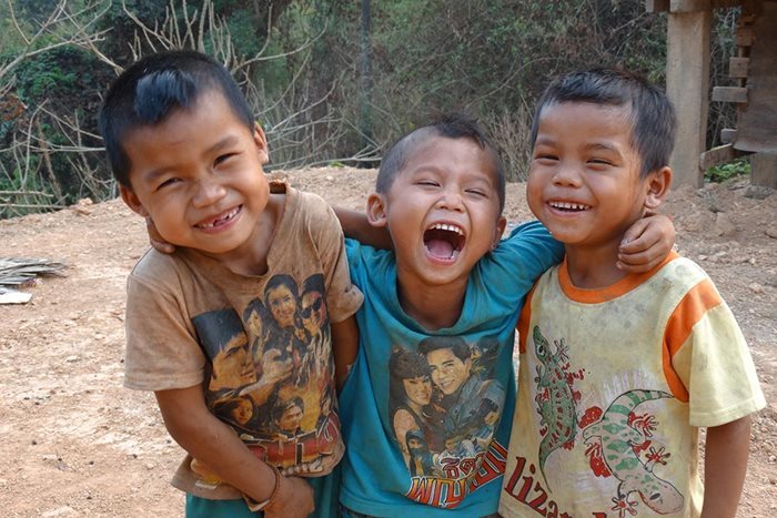 Three smiling boys in colourful t-shirts put their arms around each other in a village in Laos.