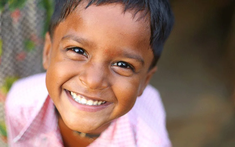 A smiling child looks toward the camera, highlighting resilience and hope amid the cycle of poverty.