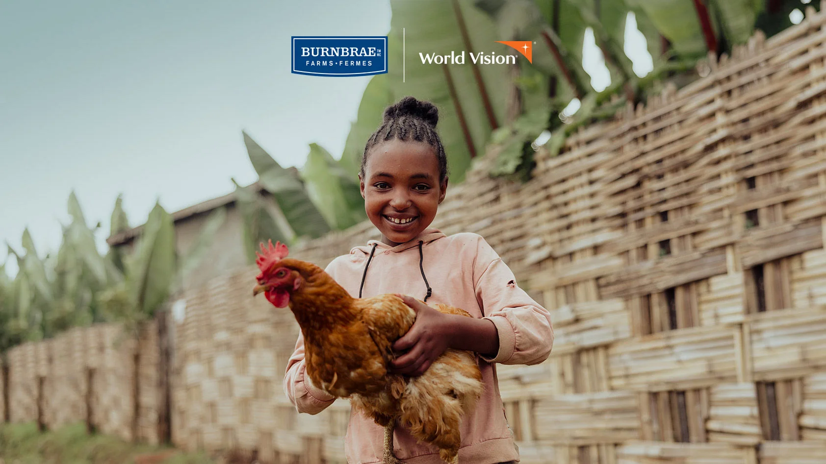 A young girl wearing a pink jacket is carrying a chicken in her arms.