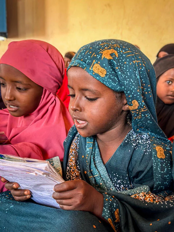 A young girl sits in her classroom in an internal displacement camp in Somalia and practices reading out loud.