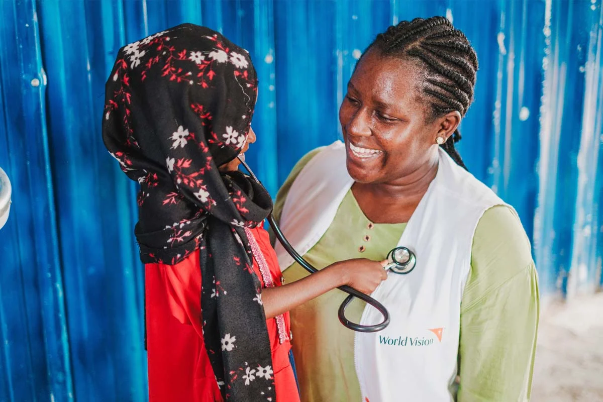 Healthcare worker smiles as displaced child checks her vitals
