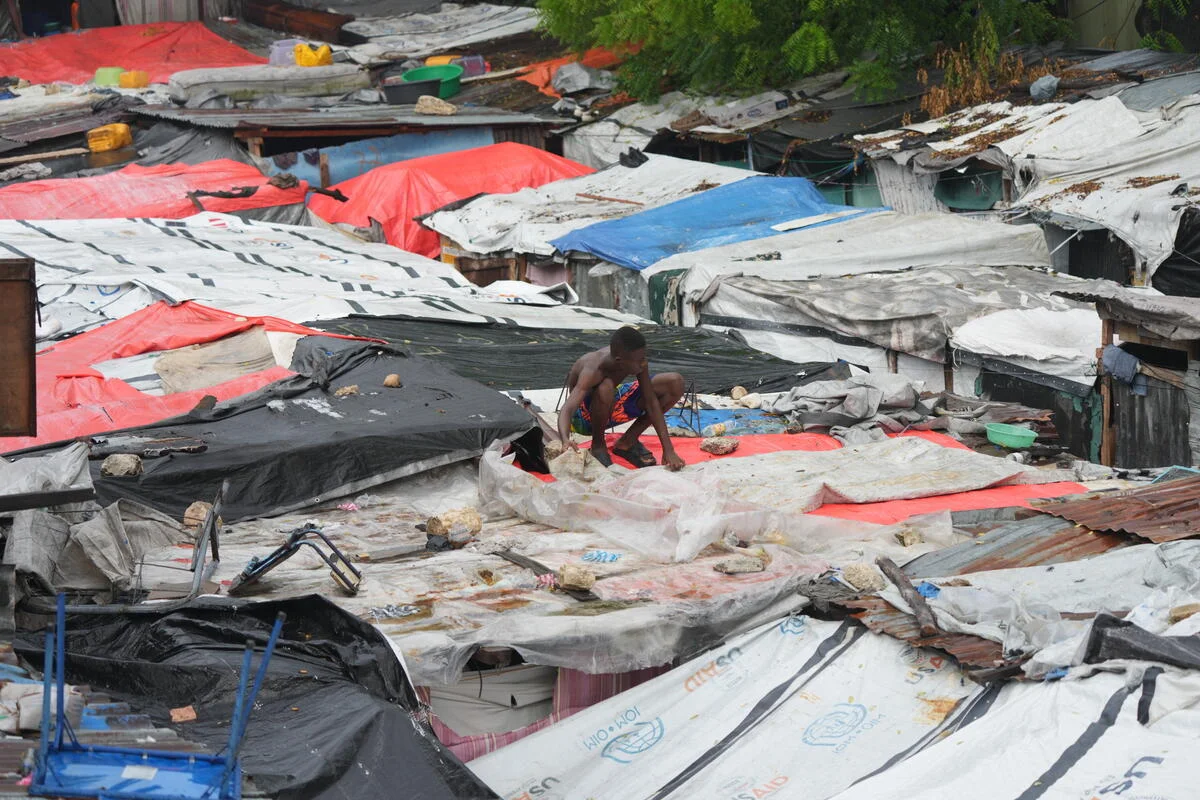 Photo Credit: Joseph Odelyn Man securing tarps on top of his shelter in Camp Domond.