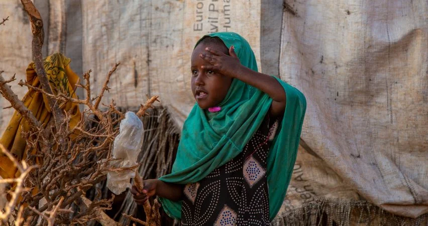 A young girl shades her eyes as she looks across the camp. Somalia, 2023