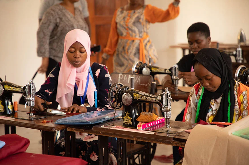 Two adolescent girls use sewing machines.