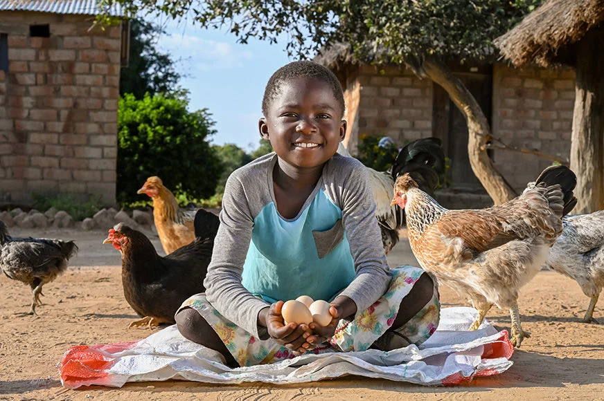 A girl is sitting on the floor, holds a handful of eggs she collected from the chickens her family raised.