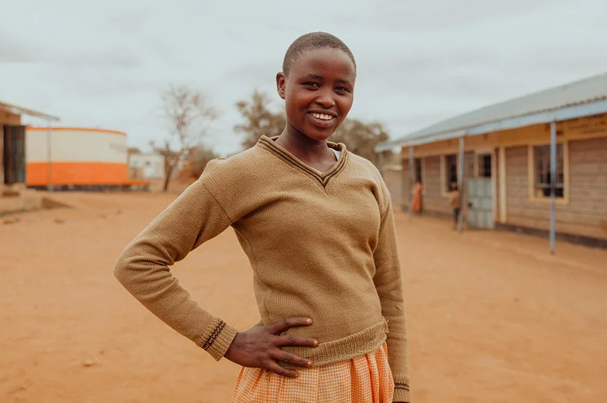 Lente, a young lady who is a sponsored child, stands in the schoolyard.