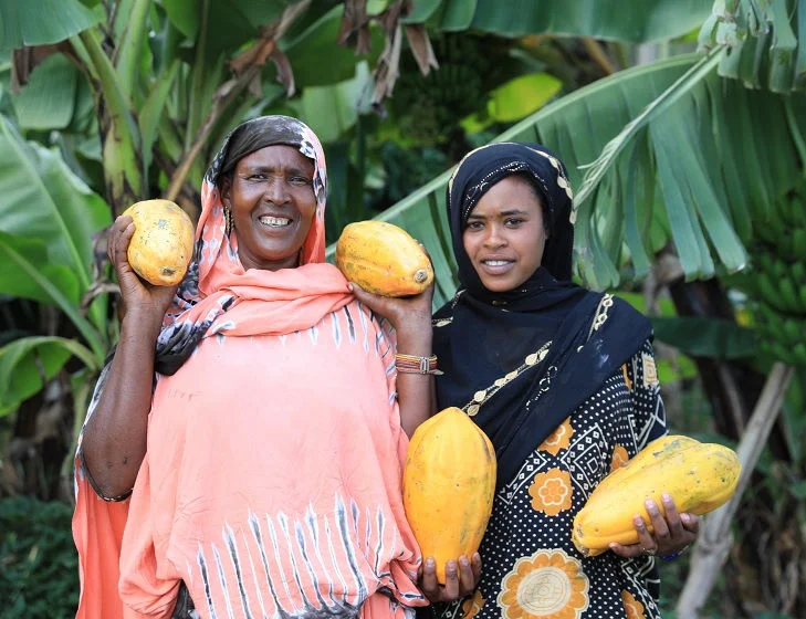 Two women hold papayas that they have grown.