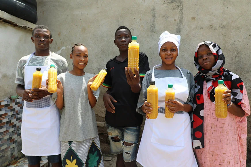 Five adolescents hold bottles of juice and smile.
