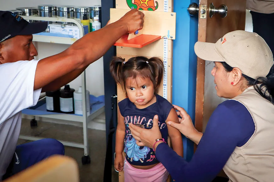 World Vision community health workers measure the height of a little girl during a check-up. (Venezuela, 2024)