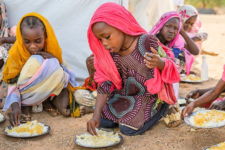 Sudanese children sit on the ground eating during a World Vision school feeding program in Farchana Refugee Camp, Chad.