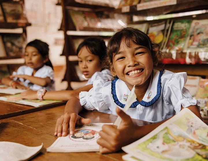 Three girls wearing school uniform are in a library reading books.
