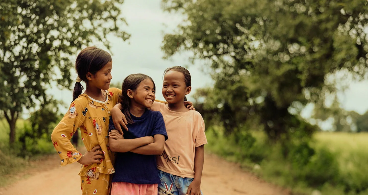 Three young girls smiling with their arms around each other.