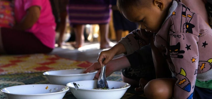 A young child eats a meal from a bowl on the floor.