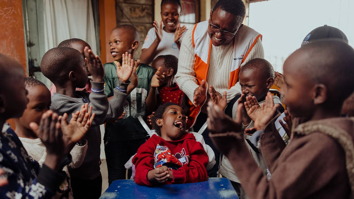 A World Vision staff member and children are clapping together.