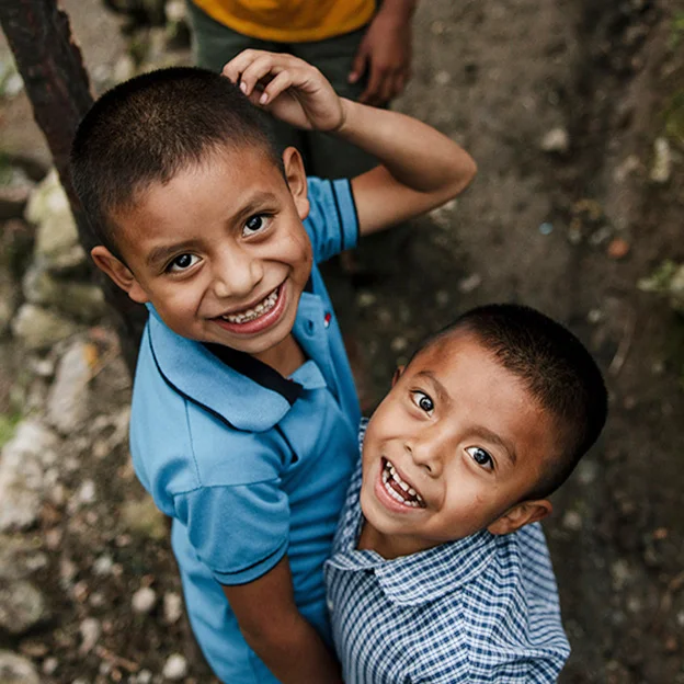 Two young boys wearing blue shirts are looking up and smiling