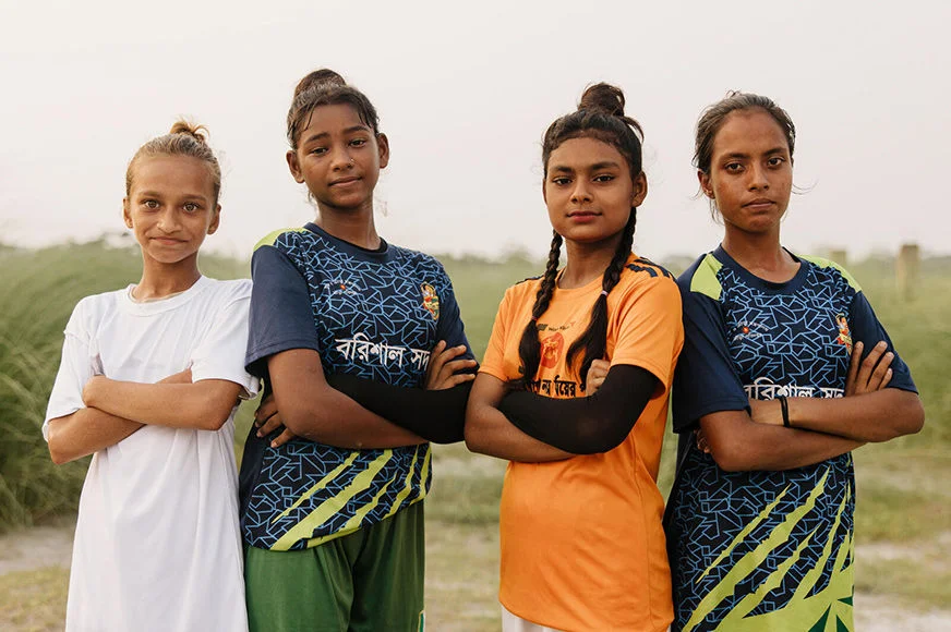 Four young girls standing at a field wearing sport shirts.