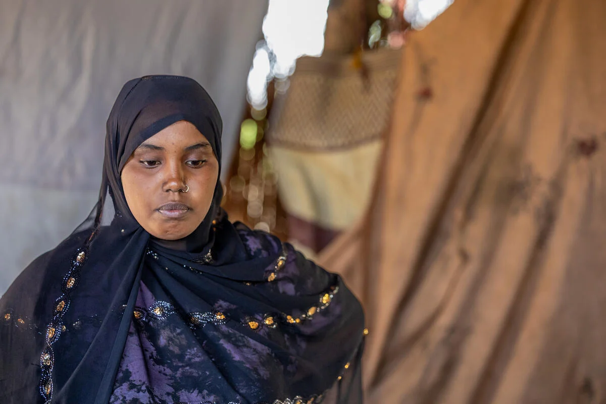 A girl looks down with a somber expression inside her family’s makeshift shelter in a refugee camp in Somalia.