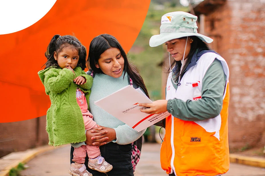 A World Vision staff member reviews documents with a mother holding a child in a rural village.