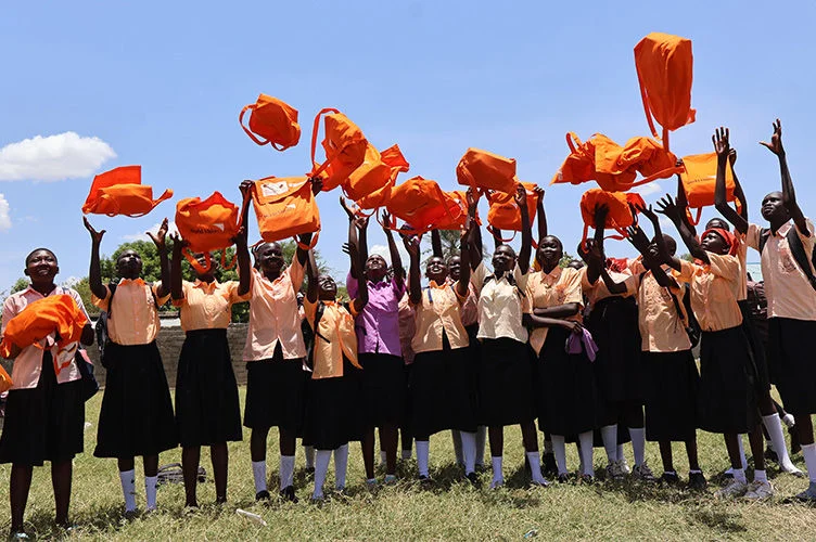 Adolescent students stand outdoors holding bright orange hygiene kits distributed by World Vision.
