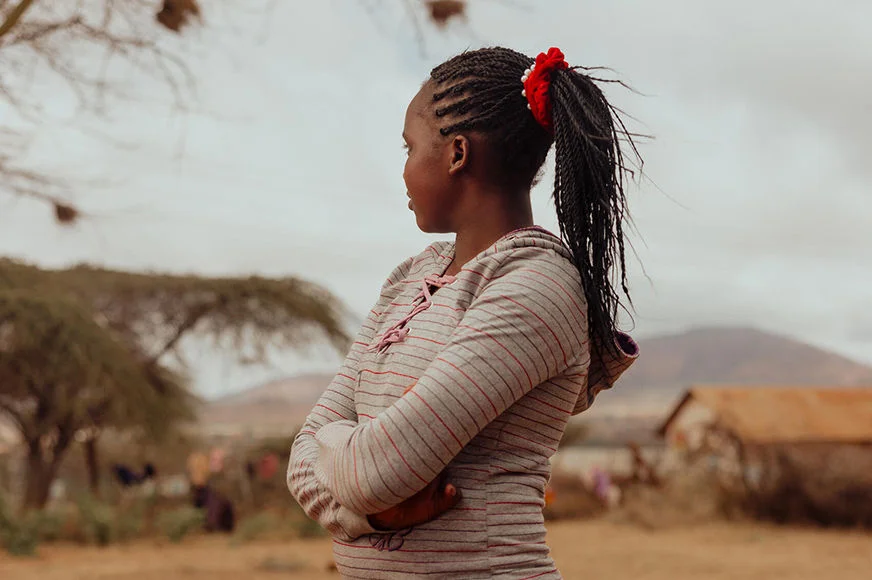 A teenage girl dressed in a gray striped sweatshirt is looking away from the camera. 