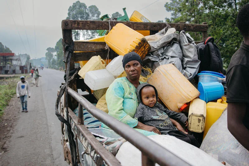Women and child sit together on the back of a truck while sheltering in place during conflict in Goma, Democratic Republic of Congo.