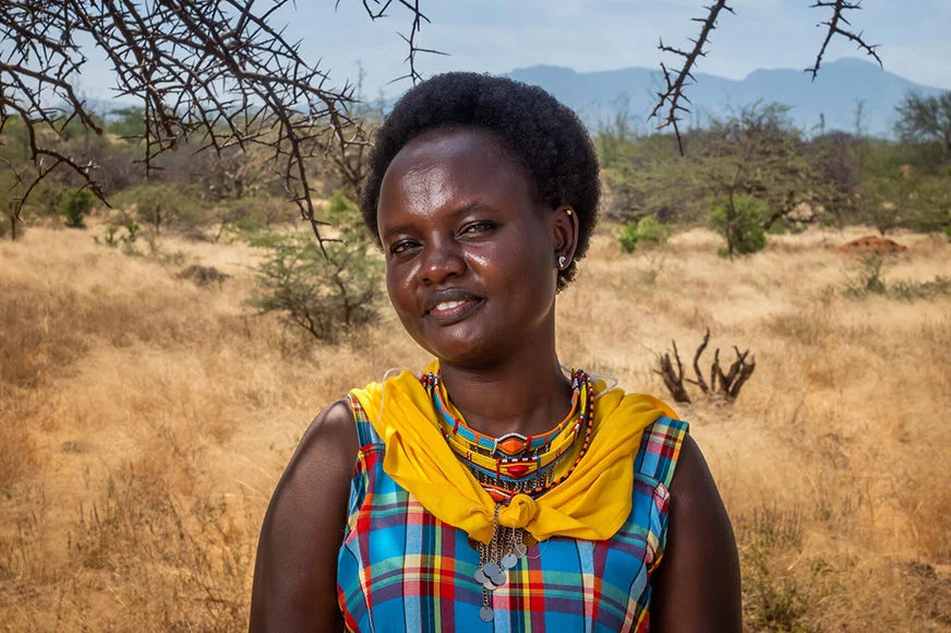 Nancy, a former sponsored child, is standing outside a field wearing a colourful dress.