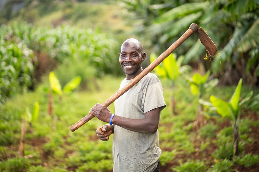 A man smiles with a farming tool.