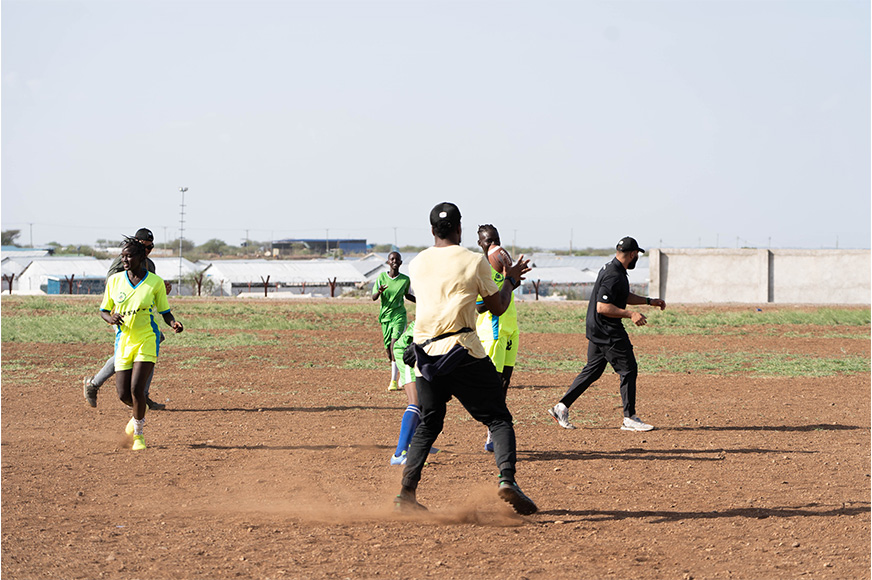 Lokombo (centre) and other CFL players play a game of football with a women's soccer team. (Kenya, 2024)