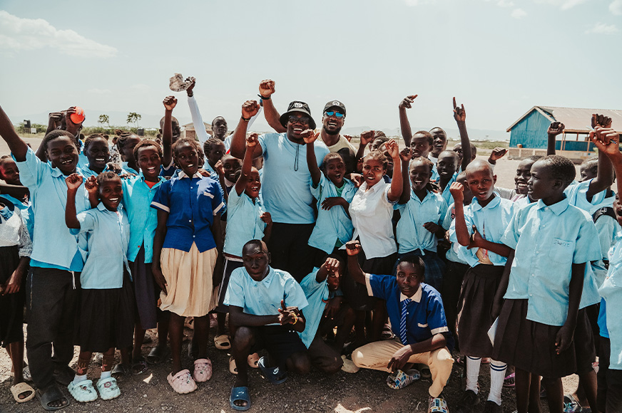World Vision Canada player ambassadors and members of the Kakuma Peace Club cheer with their hands in the air. (Kenya, 2024)