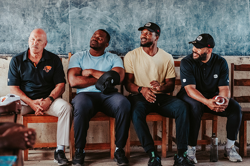 Lokombo (centre-right) with fellow football players sit in front of a chalkboard in a school in Kakuma. (Kenya, 2024)