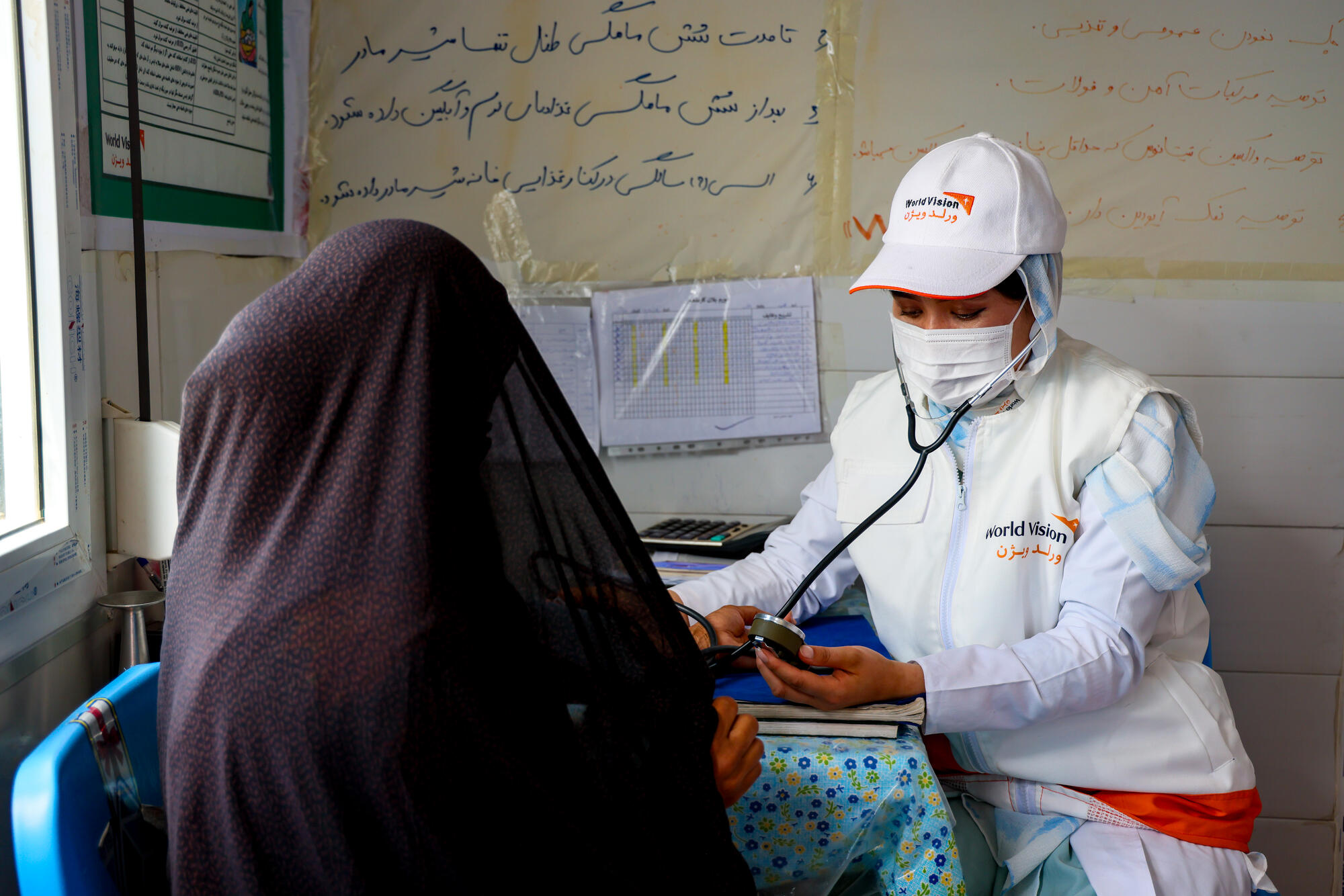 In Afghanistan, a woman in an orange and white vest provides care to her female patient.   