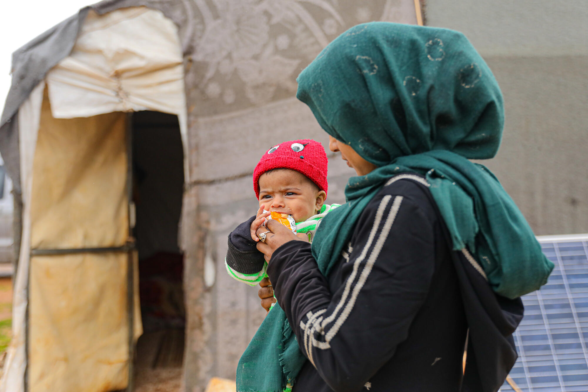 A woman holds a seven-month-old baby, providing supplemental feeding.  
