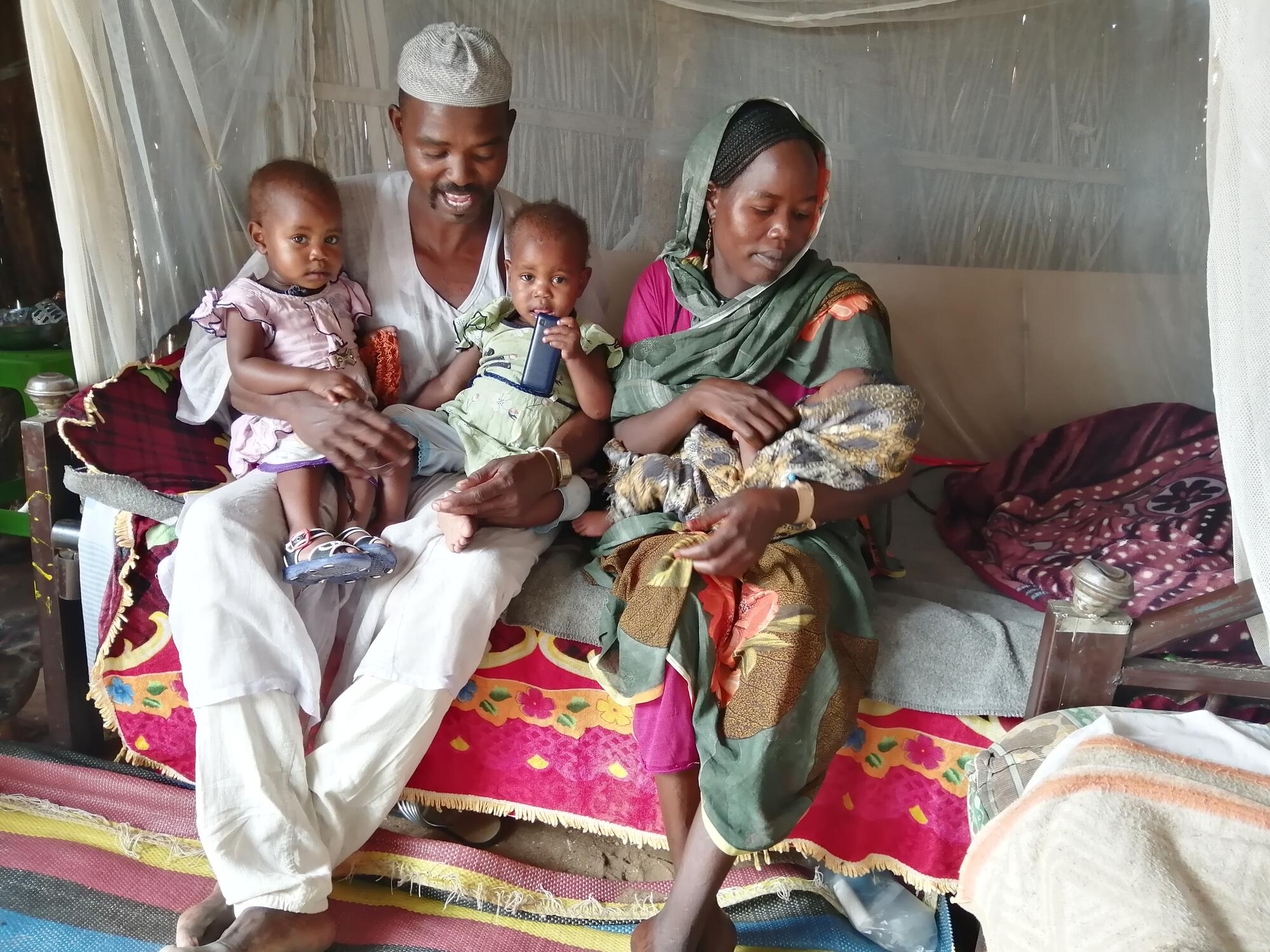 A woman and man hold two babies and one infant between them.  