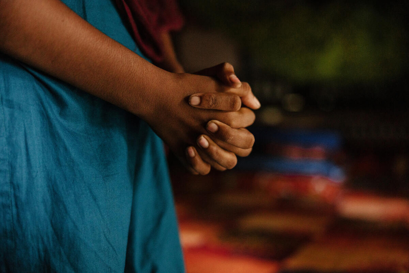 A 14-year-old girl clutches her hands in front of her. We see just her dress and her hands. 