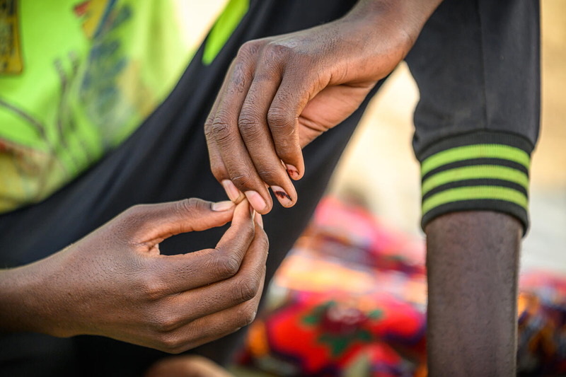 We see the close-up of a boys hands touching as he sits on the ground. 